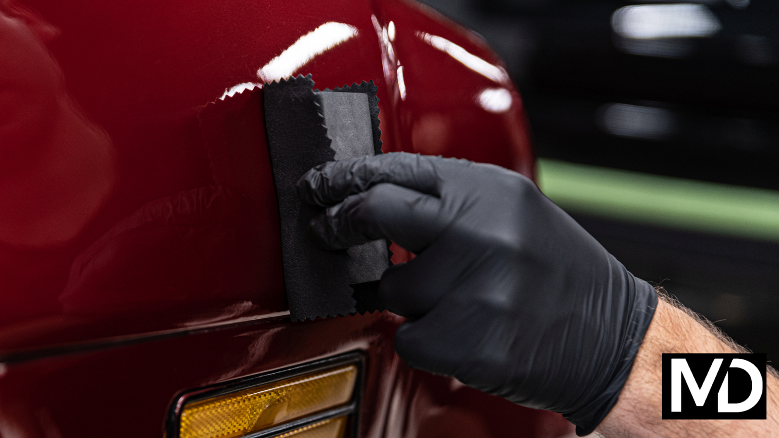 a person wearing black gloves polishing a red car